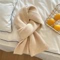 Detail eines cremefarbenen Strickschals mit Rippkanten und Zierknopf auf weißem Bettzeug - Beige