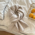 Detail eines beigen Strickschals mit Goldknopf auf weichem weißem Bettzeug - Graubeige
