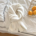 Detail eines weichen elfenbeinfarbenen Strickschals mit goldenem Knopf und Rippenstruktur - Weiß
