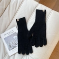Detail of black knit gloves with ribbed cuffs and leather label on a cozy sofa - One Size / Black