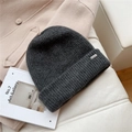 Detalle del gorro de punto gris oscuro con etiqueta metálica sobre abrigo beige - Talla única / Negro y Gris