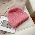 Detalle de gorro de punto rosa con textura suave y etiqueta metálica rectangular con logo - Talla única / Rosa