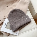 Primer plano detallado del gorro de punto marrón con placa de metal sobre abrigo lana - Talla única / café