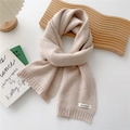 Detail of soft beige knitted scarf with Cashmere label on a minimalist white desk - Beige