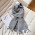Detailed view of grey knit scarf texture with tassel fringe and metal logo tag - Light Gray