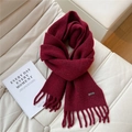 Détail d'une écharpe en maille bordeaux avec franges et étiquette argentée sur cuir doux - Bordeaux