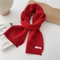 Detail of red knit scarf with cashmere label and ribbed edge on a white decorative table - Red