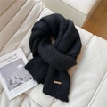 Detail of soft black knit scarf with branded tag on white textured sofa background - Black