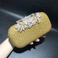 Close-up of gold rhinestone evening clutch featuring silver floral clasp with crystals - Gold Rhinestone White Flower
