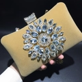 Macro detail of velvet evening bag featuring sparkling rhinestone sunflower and gold chain - Camel