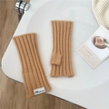 Nahaufnahme camelfarbene Strickstulpen mit vertikalem Rippmuster und einem weißen Webetikett - Camel