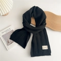 Close-up of black knitted scarf featuring a white woven label with vertical textures - Black