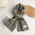 Close-up of sage green ribbed knit scarf with a minimalist woven emo brand label - Light Green