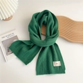 Close-up of dark green ribbed knit scarf with a white woven label on white background - Dark Green