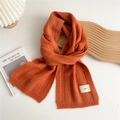 Detail of orange ribbed knit scarf with minimalist emo woven label on textured fabric - Orange