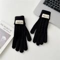 Detail of black cable-knit touchscreen gloves with brand tag on a modern desk setup - Black