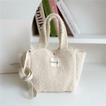 Close-up of fuzzy cream tote bag with fabric strap and rectangle brand label - Beige