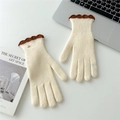 Close-up of cream knit gloves with brown wavy edges and a gold logo button detail - Milk White Contrast Scalloped Edge