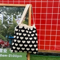 Detail of a black knitted heart pattern tote bag hanging on a display stand in a street setting - Black Heart Pattern