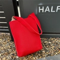 Detailed close-up of bright red pleated knit tote bag with vertical stripes in outdoor setting - Red