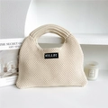 Detalle de bolso tote de punto crema con textura de gofre y etiqueta en un soporte minimal - Beige