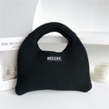 Close-up of a black knitted tote bag with a minimalist brand label on white desk - Black