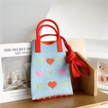 Detail of blue knitted bag with heart patterns and red handle on a rustic wooden stand - Blue Heart