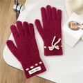 Detail der dunkelrosa Strickhandschuhe mit weißer Schleife und Stoff-Markenetikett - Rosalila