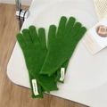 Macro shot of green knitted wool glove with white logo tag on a textured surface - One Size / Dark Green