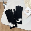 Detail of black knit gloves with soft white pom poms and a branded woven wrist label - One Size / Black