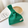 Detailansicht der grünen Strickhandtasche mit Logo-Patch auf einem weißen Beistelltisch - Dunkelgrün