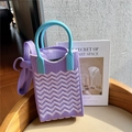 Detail of purple wavy knit phone bag with blue round handle on a wooden surface - Purple Texture