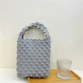 Detail of grey knitted tote bag featuring a 3D bubble texture and wavy handle design - Gray