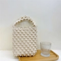 Detail of cream knitted handbag with 3D popcorn texture and scalloped handles on a bamboo tray - Beige