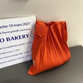 Detailed view of an orange pleated knit tote bag with a ribbon tie and woven label - Orange Red