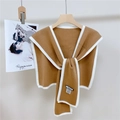 Dettaglio dello scialle in maglia marrone con bordo bianco a contrasto su gruccia in legno - Cammello