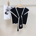 Dettaglio dello scialle in maglia nera con bordino bianco appeso a una gruccia in legno - Nero Classico