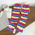 Close-up van gebreide armwarmers met regenboogstrepen en merklabel op houten tafel - Eén maat / Regenboog blauw