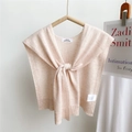 Detail view of a beige knit shawl accessory featuring a minimalist neck label on a wooden hanger - Nude