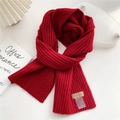 Dettaglio sciarpa in maglia rossa con toppa in pelle e etichetta su superficie bianca - Rosso