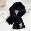 Macro shot of black ribbed knit scarf texture with a brown leather label on white background - Black