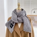 Detailed texture of grey chunky knit scarf with woven cable pattern and branded label - Gray
