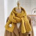Close-up of yellow chunky knit scarf with vintage cable pattern and branded fabric label - Yellow