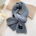 Chic grey knitted scarf with black brand tag on stylish wooden display background - Gray
