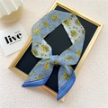 Narrow blue floral silk scarf tied in a bow on a black display board for women - Yellow Plum Blue