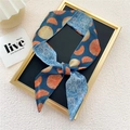 Narrow silk scarf with orange fruit prints and blue patterns tied on a luxury display - Blue Orange