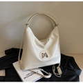 Große cremeweiße Hobo-Tasche mit M-Metalllogo und Kettengurt auf schwarzem Lederhintergrund - Gebrochenes Weiß