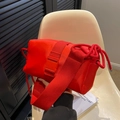 Rode nylon crossbodytas met brede schouderband en trekkoorddetail op een witte stoel - Rood