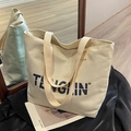 Bolso tote de lona blanco roto con letras de logo negro en un ambiente minimalista - Blanco Roto
