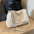 Elegant cream tote bag with ruched design and silver chain strap on stone surface - White